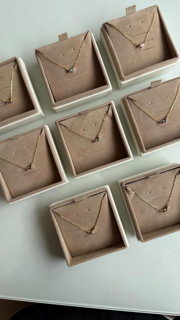 Gold necklaces with various colored gemstones displayed in individual tan jewelry gift boxes.