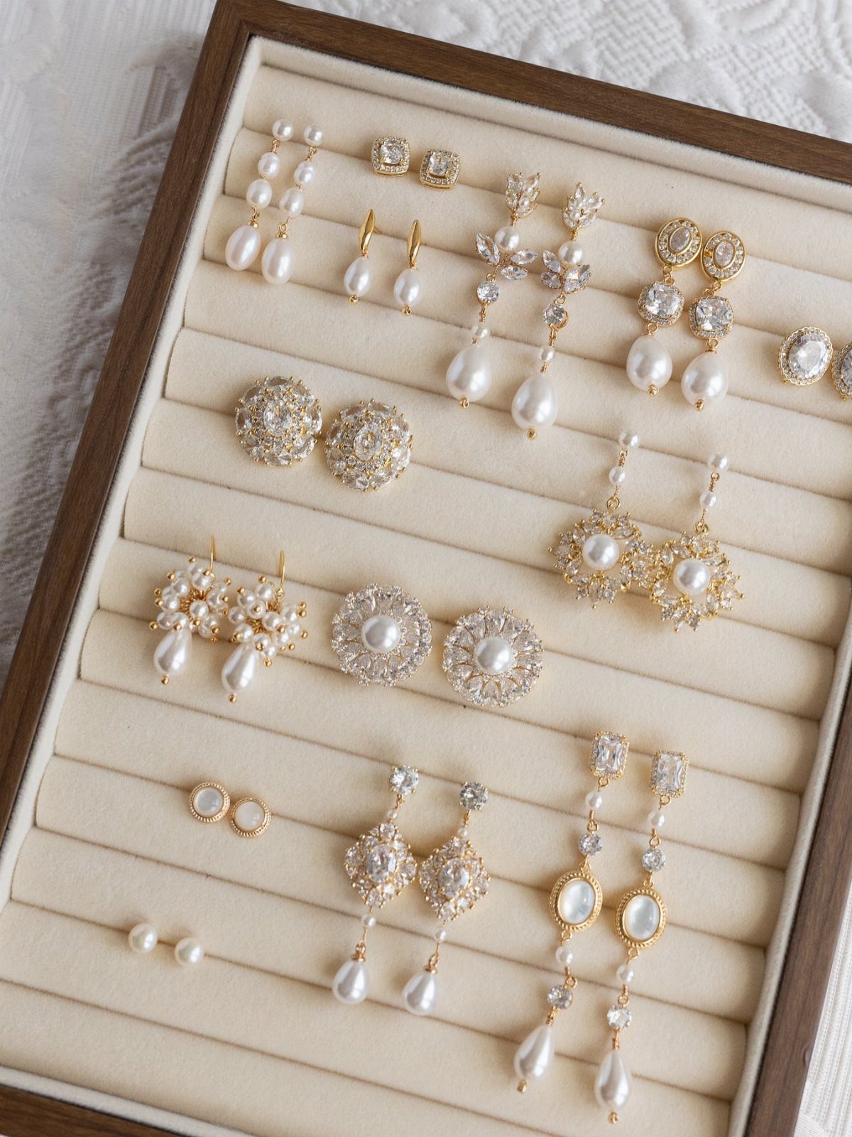 Various gold and pearl earrings arranged neatly inside a wooden jewelry organizer tray.