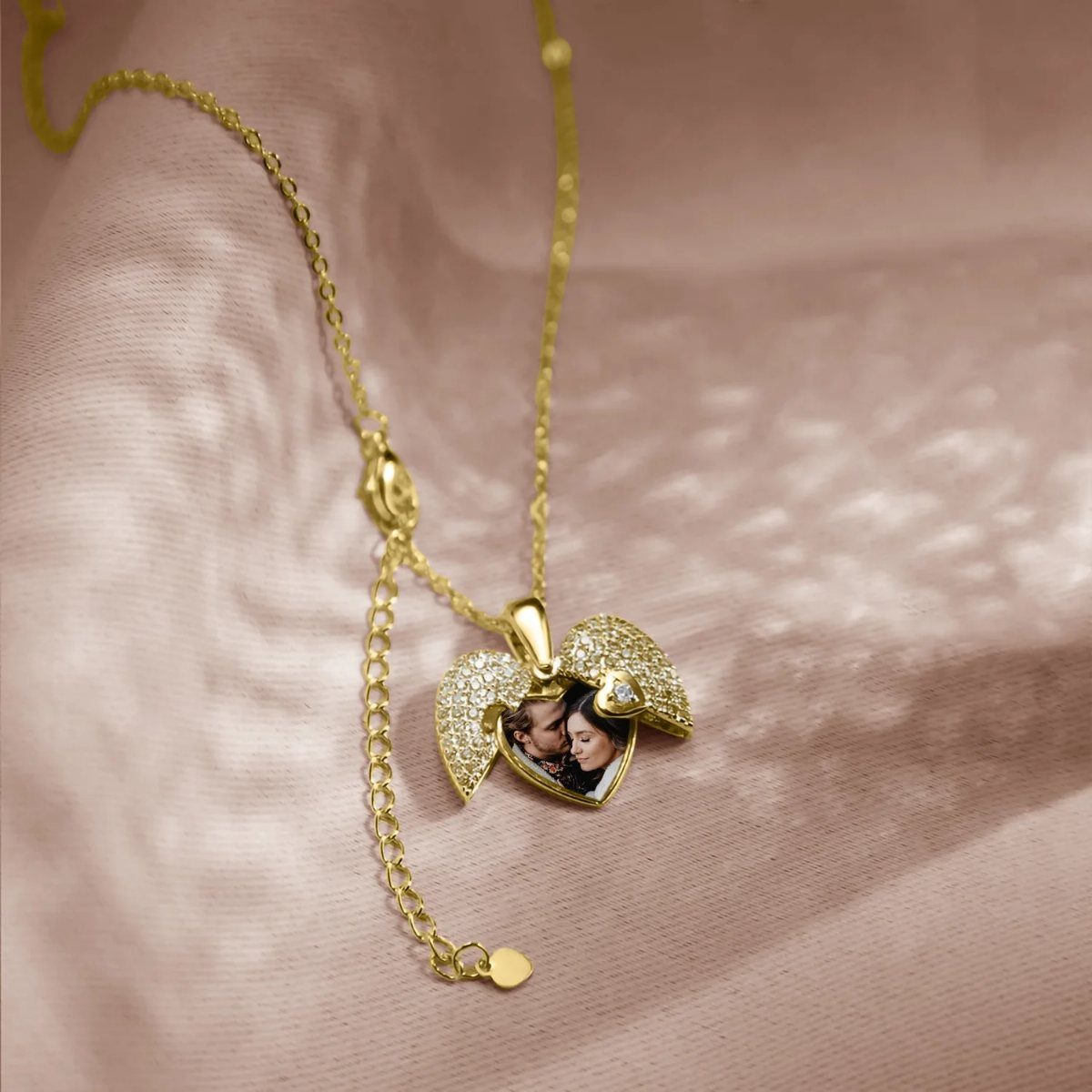 Gold heart-shaped locket necklace containing a small photograph of a couple on pink fabric.