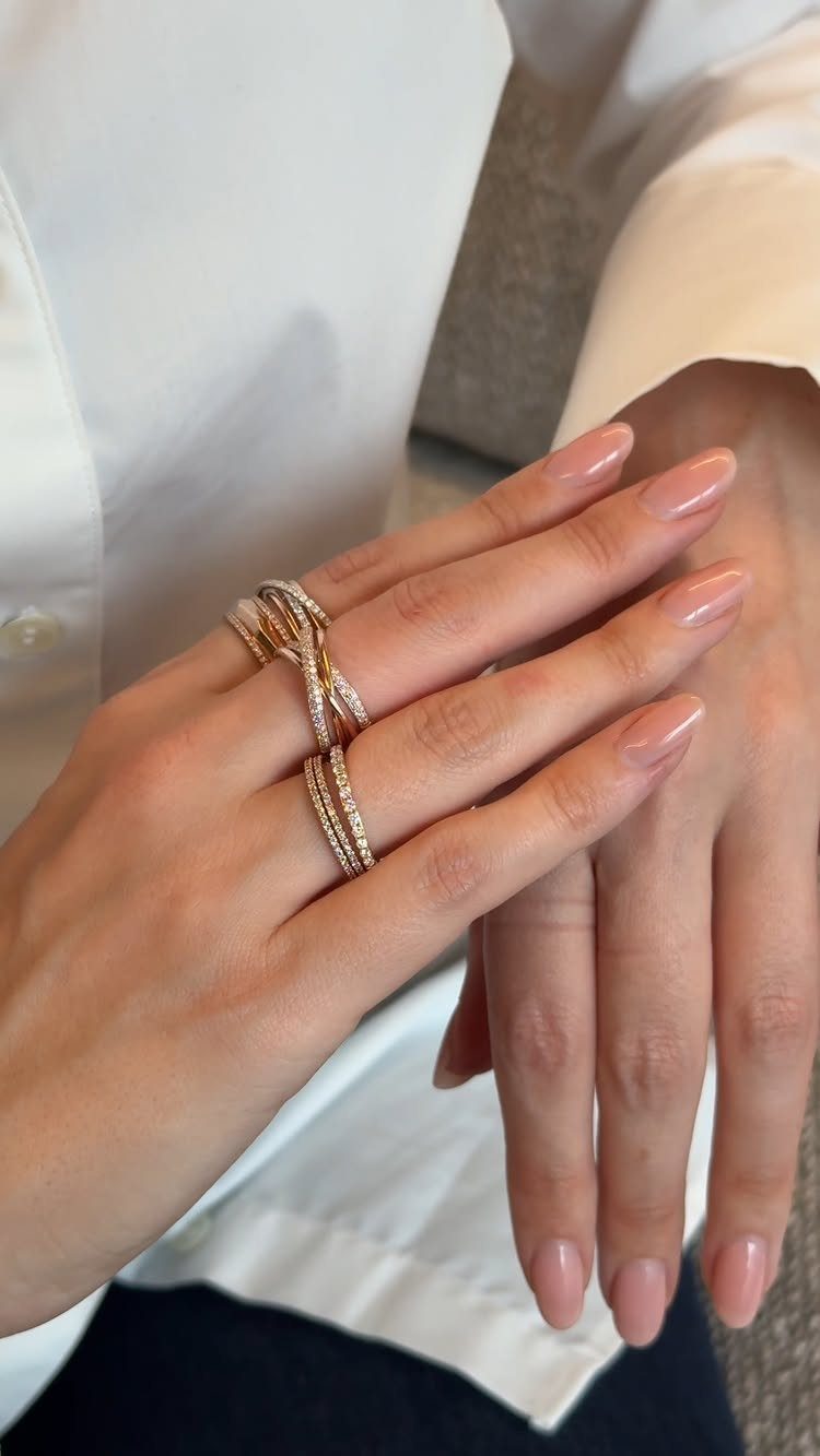 Hands with manicured nails wearing multiple stacked gold diamond rings.