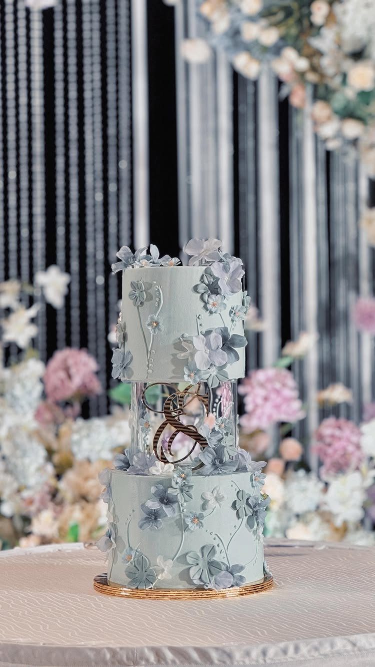 Light Blue Wedding: 8 Ideas From Cake to Tulle Runner 1 A two-tier light blue wedding cake decorated with intricate sugar flowers and gold accents.