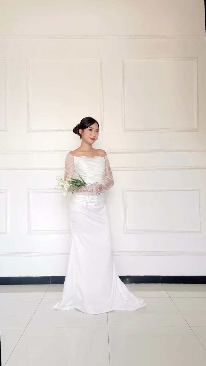 A woman wearing a white wedding dress with delicate lace sleeves holding a bouquet.