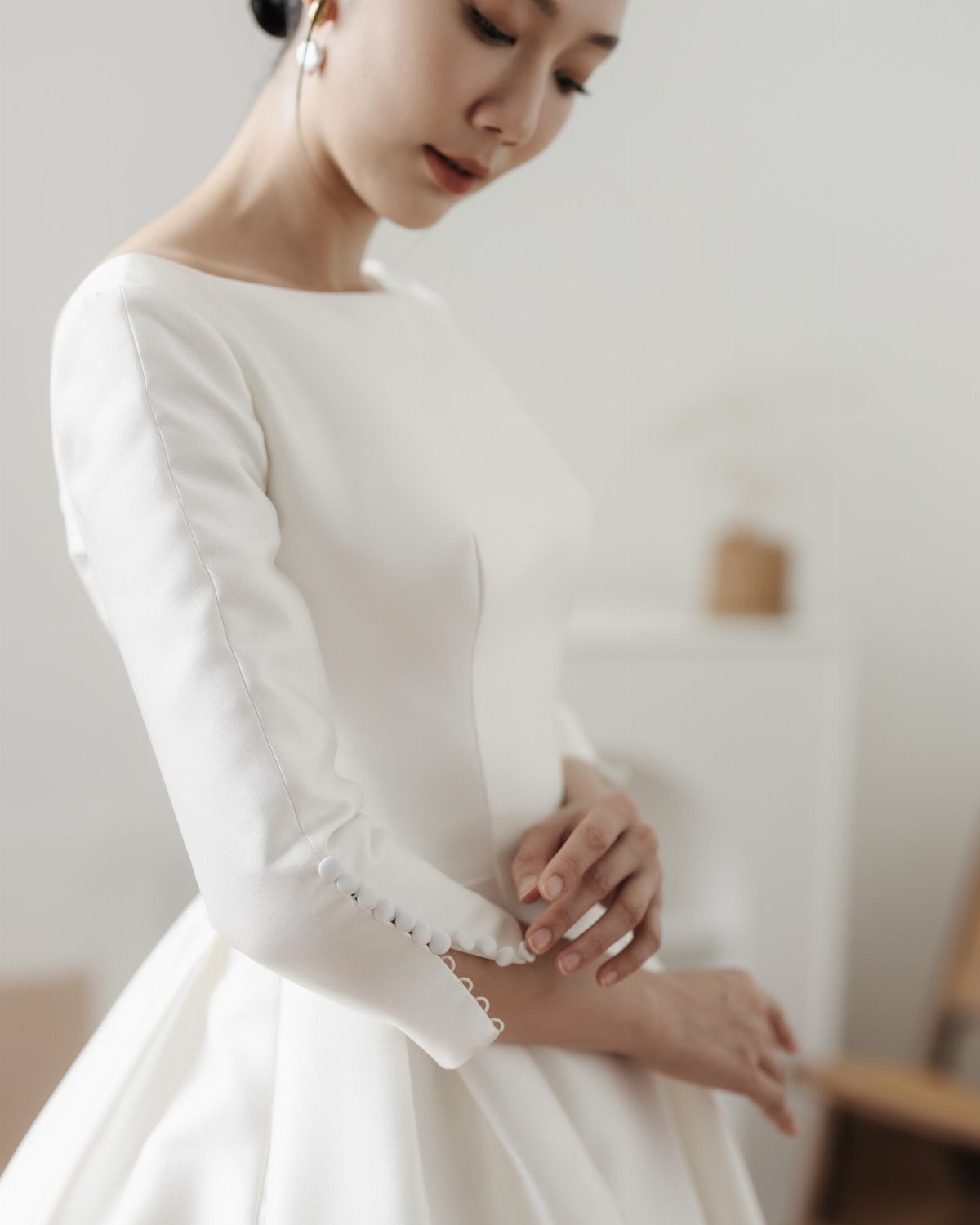 A woman wearing a minimalist white long-sleeved wedding dress with buttoned cuffs.