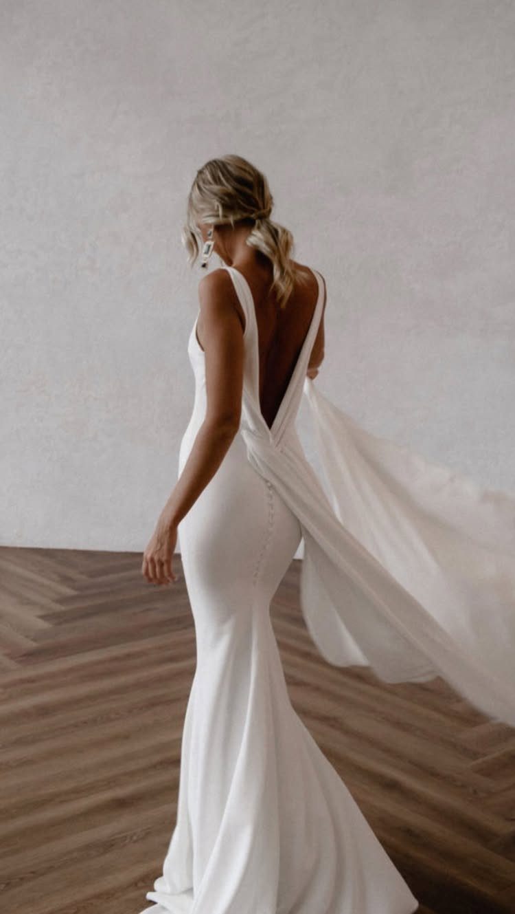 A woman in a sleek white minimalist wedding dress with a deep V-back and flowing train.