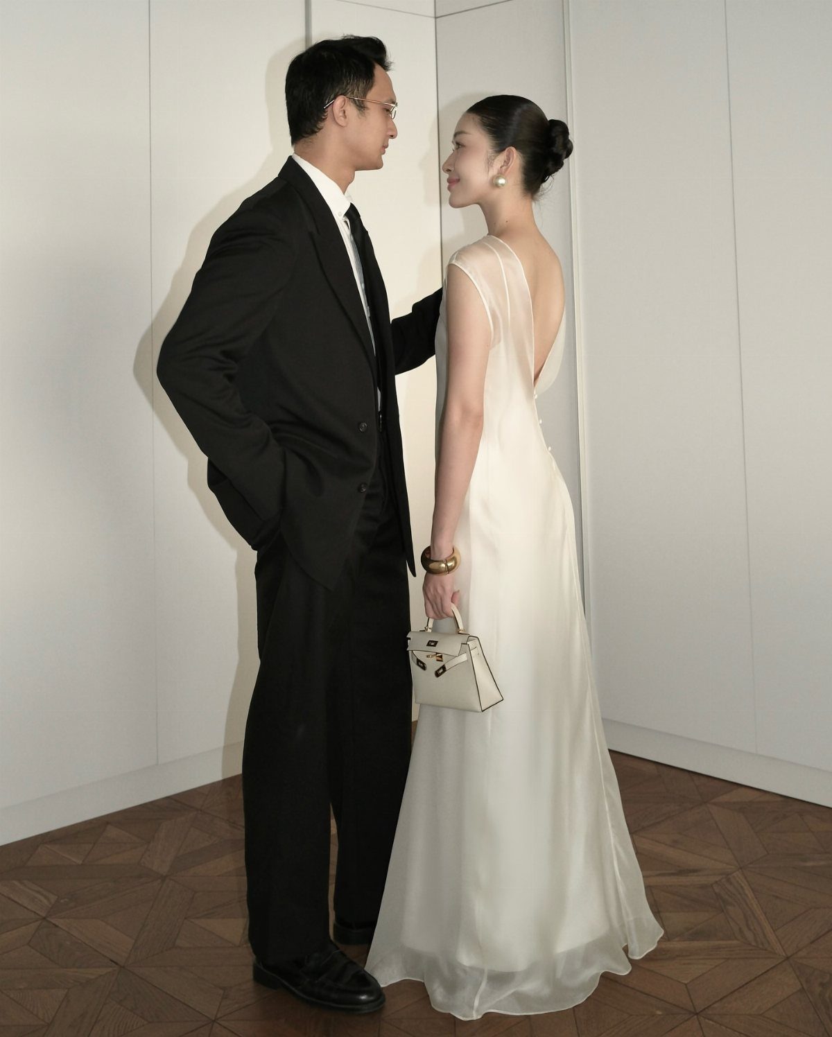 A woman in a minimal white V-back wedding dress standing with a man in a black suit.
