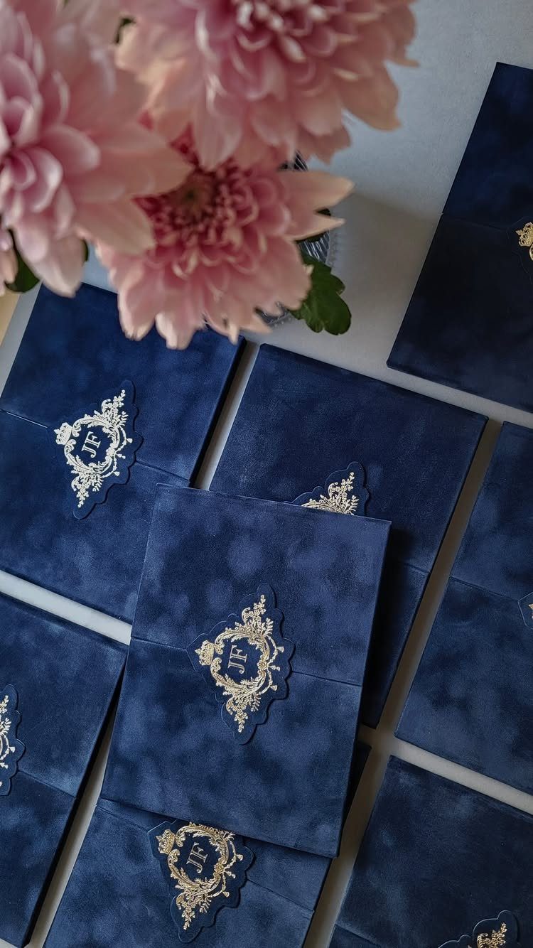 Navy blue wedding invitations with gold crests arranged near pink flowers.