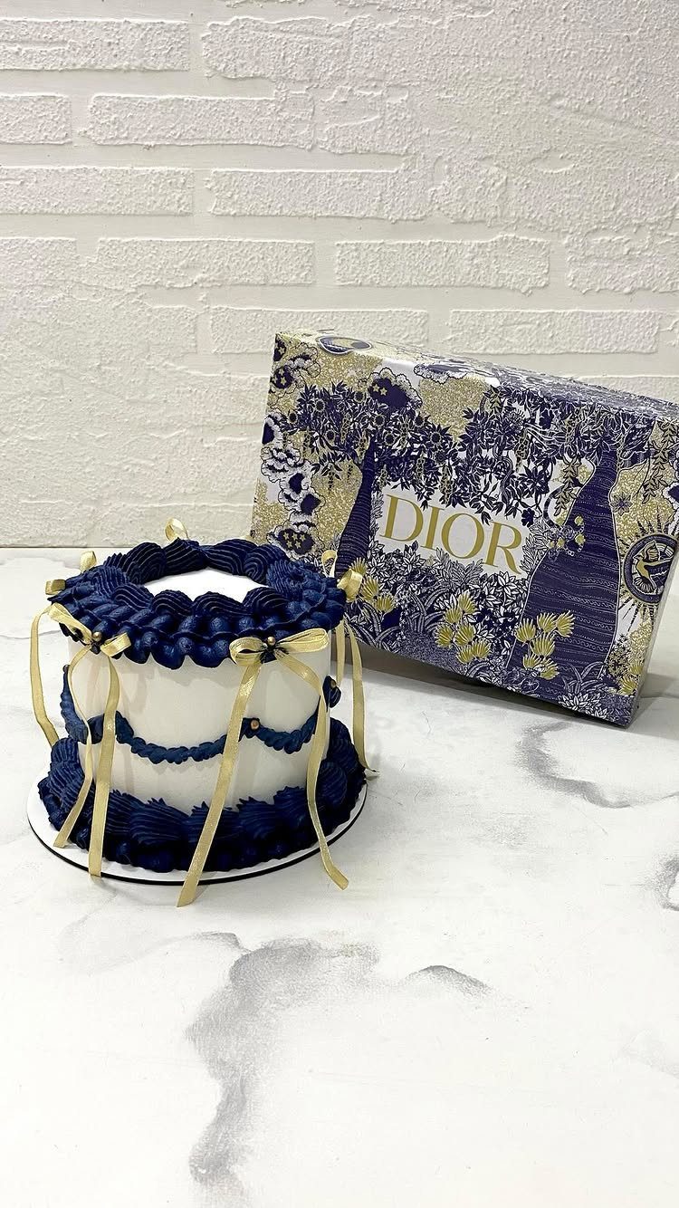 White cake with navy blue frosting ruffles and gold ribbons sitting next to a Dior box.