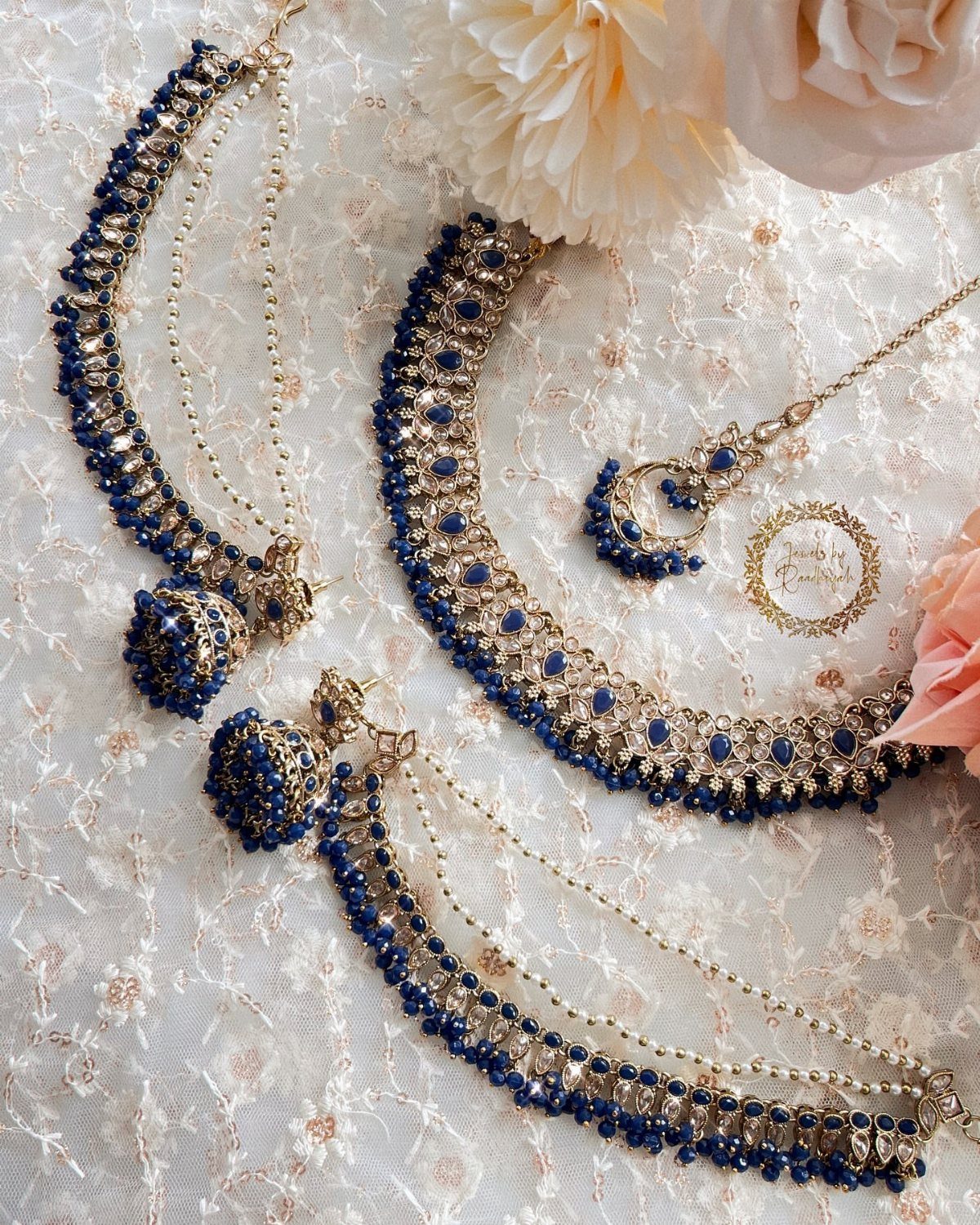 Blue kundan necklace set with gold detailing resting on white lace fabric with flowers.