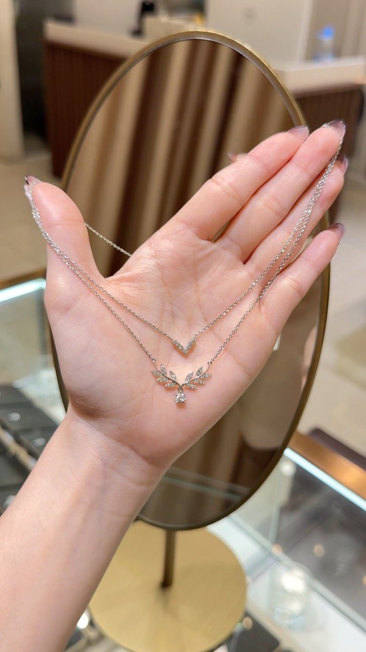 A hand holding a delicate silver layered necklace with small floral and V-shaped pendants.