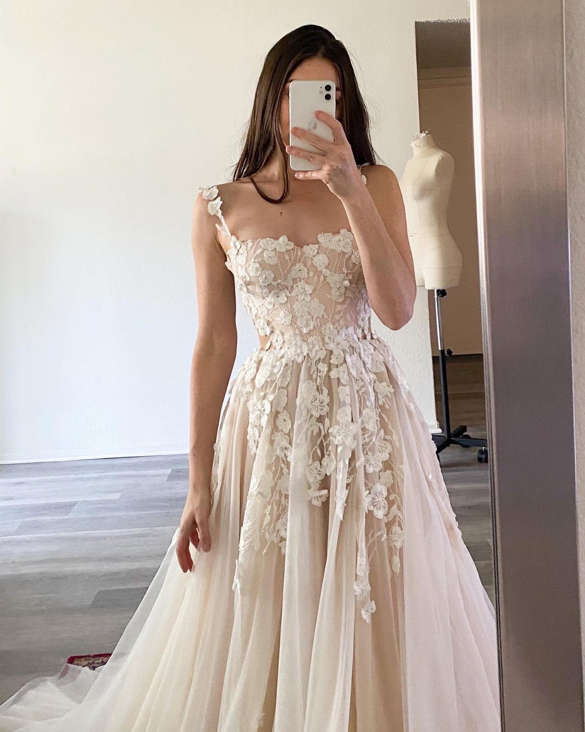Woman in a floral lace off-white wedding dress taking a mirror selfie.