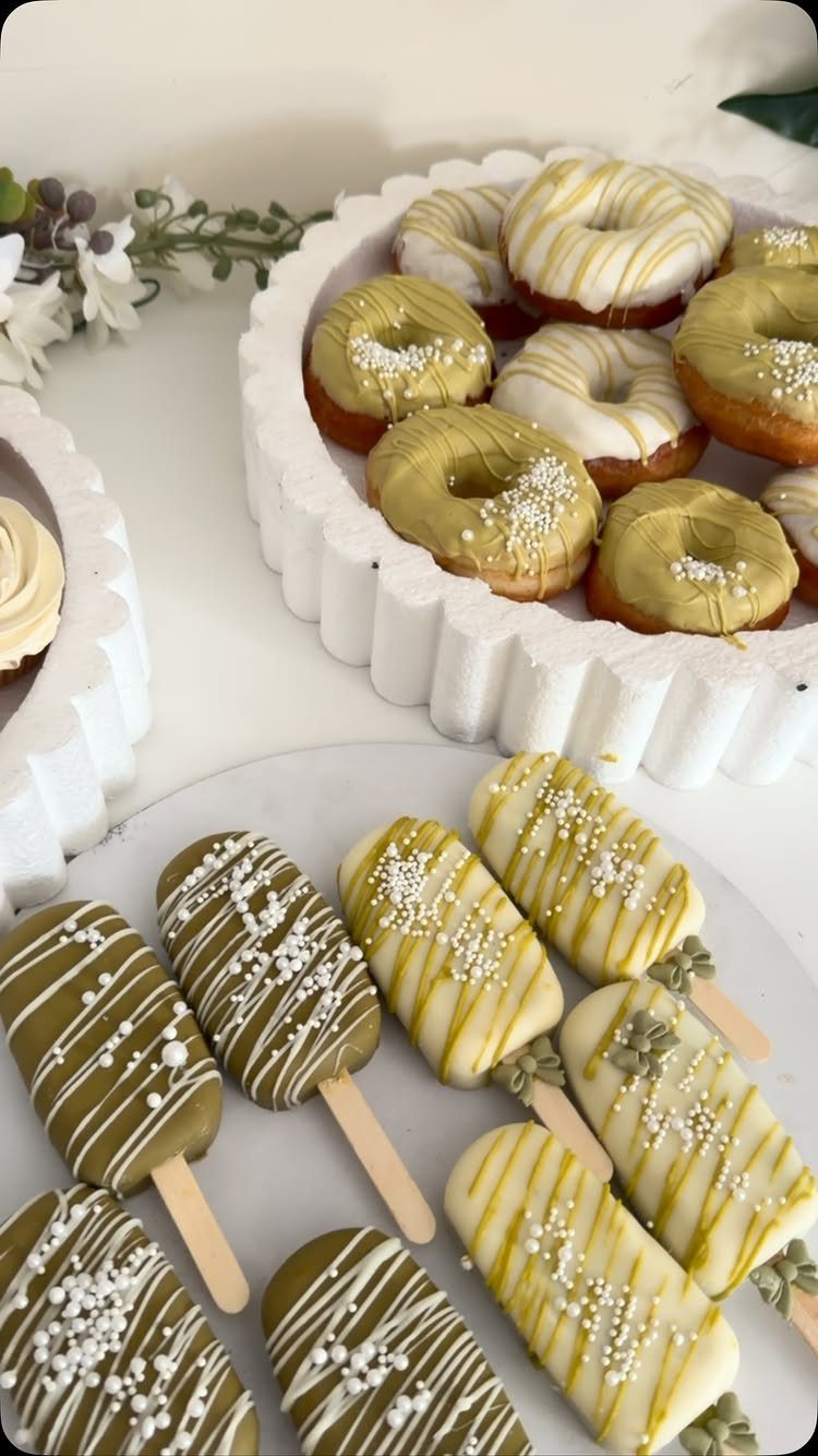 Assorted donuts and cake pops decorated with olive green and white icing and sprinkles on white platters.