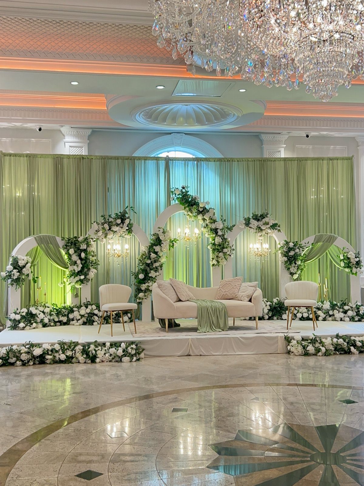 Olive green drapes serve as a backdrop for a wedding stage with white floral arches.