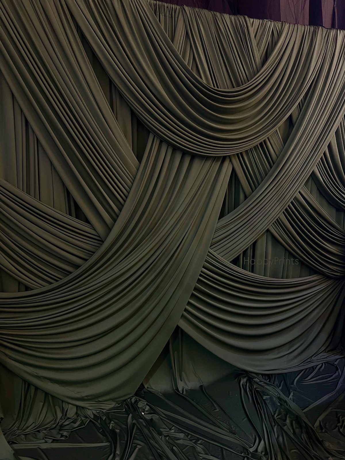 Draped olive green fabric arranged in elegant, flowing swags and textured folds.