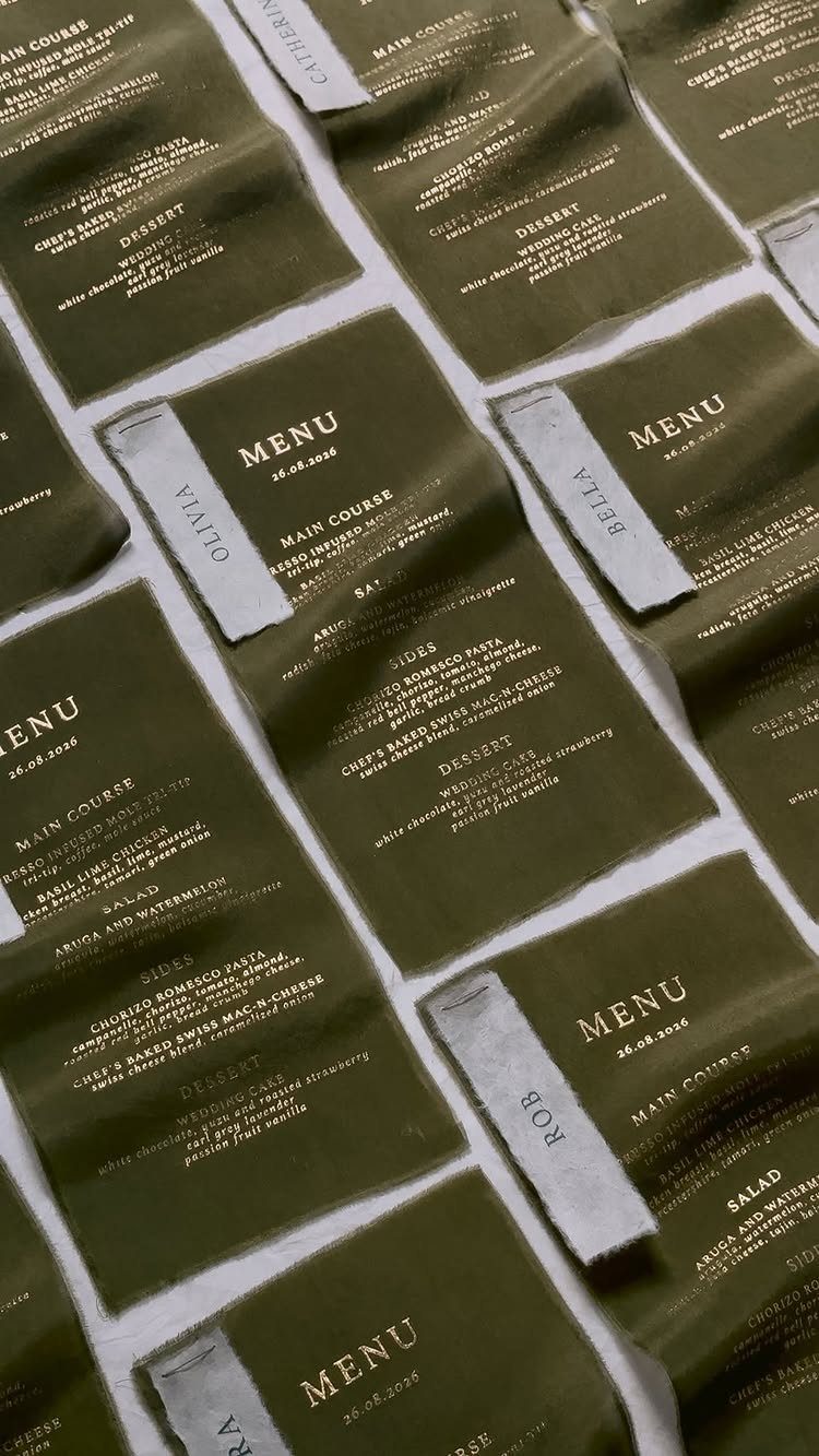 Olive green wedding menus with gold lettering and grey name tags arranged on a table.