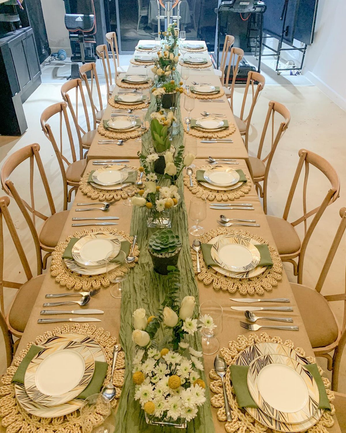 A long wedding table set with olive green gauze runners and white floral centerpieces.