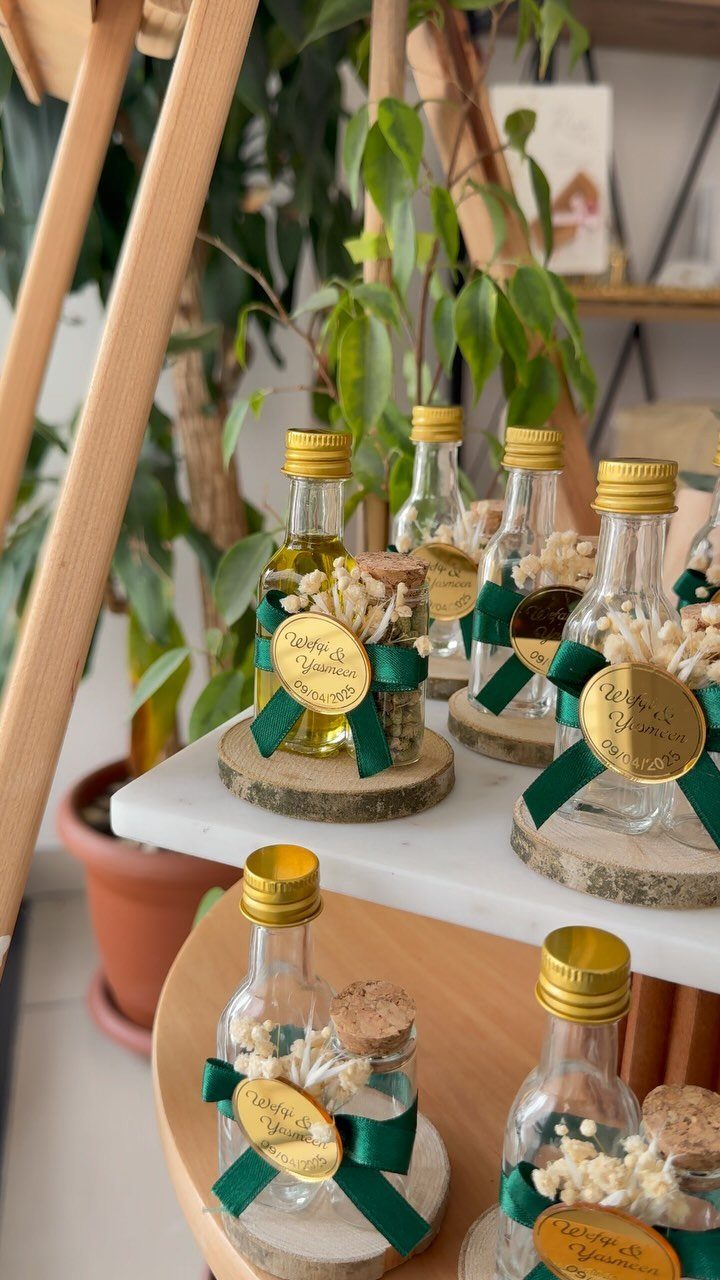 Miniature glass bottles of olive oil with green ribbons and gold labels on wooden coasters.