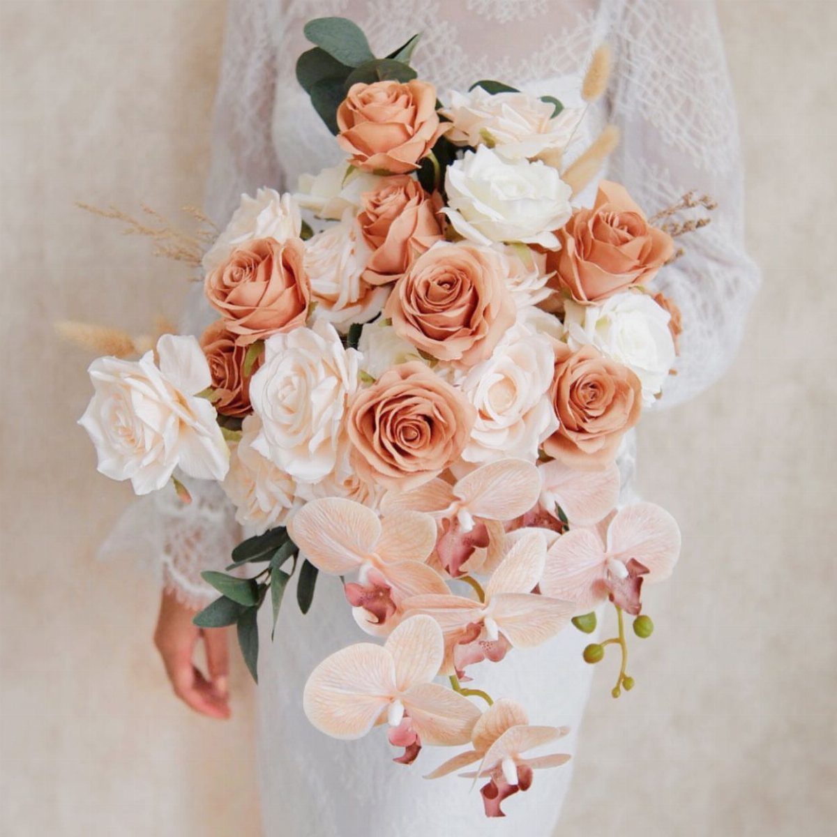 7 Orchids Bouquet Wedding Ideas for Every Style of Ceremony 6 A wedding bouquet of peach roses and pale pink orchids held against a white lace dress.