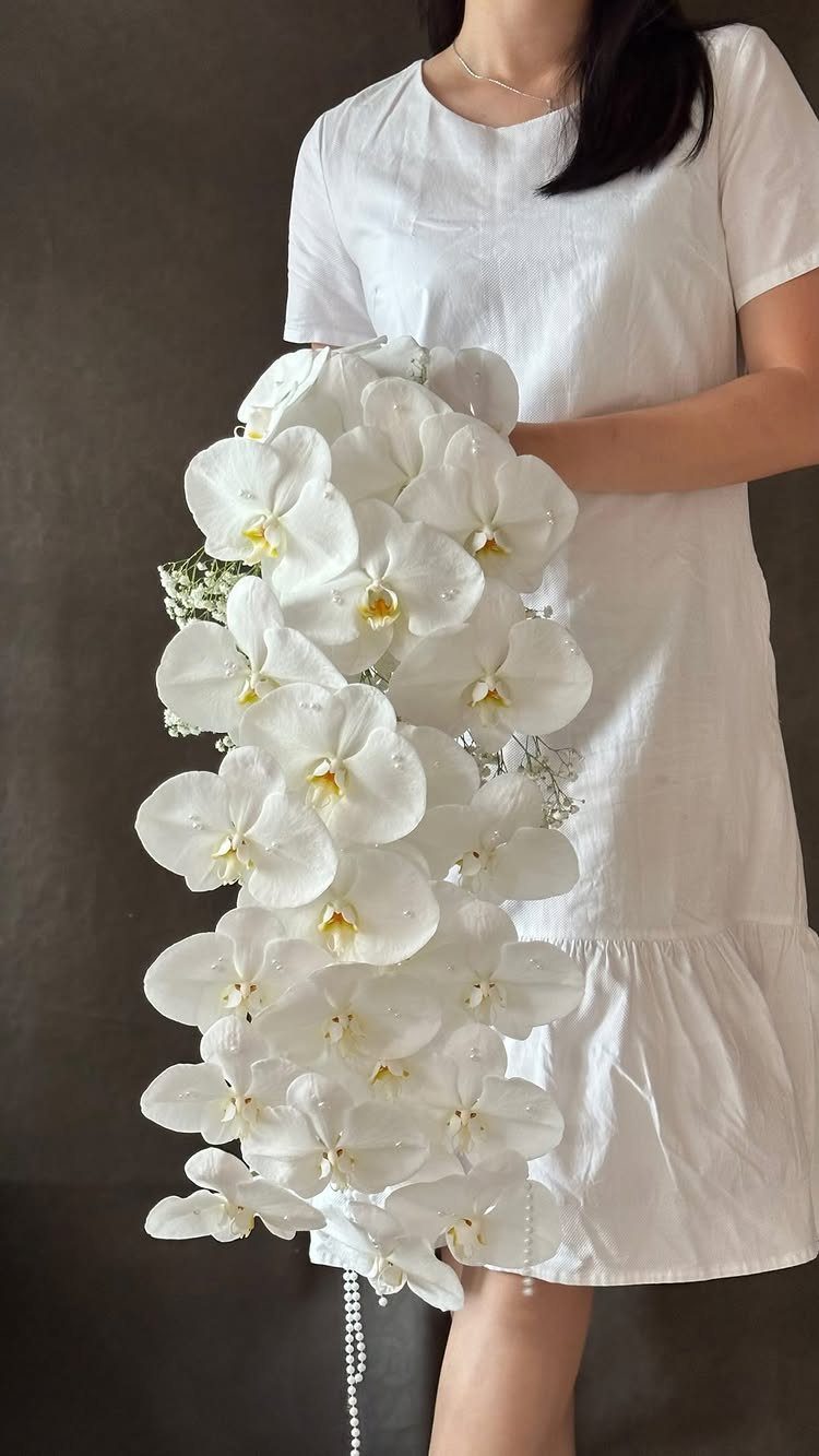 7 Orchids Bouquet Wedding Ideas for Every Style of Ceremony 1 A person holding a large cascading bouquet of white Phalaenopsis orchids against a dark background.