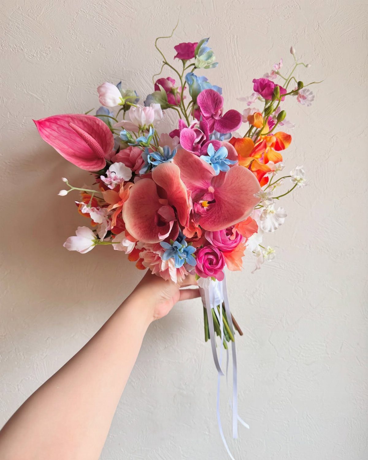 7 Orchids Bouquet Wedding Ideas for Every Style of Ceremony 7 A hand holding a colorful bouquet of pink, orange, and blue orchids and roses.
