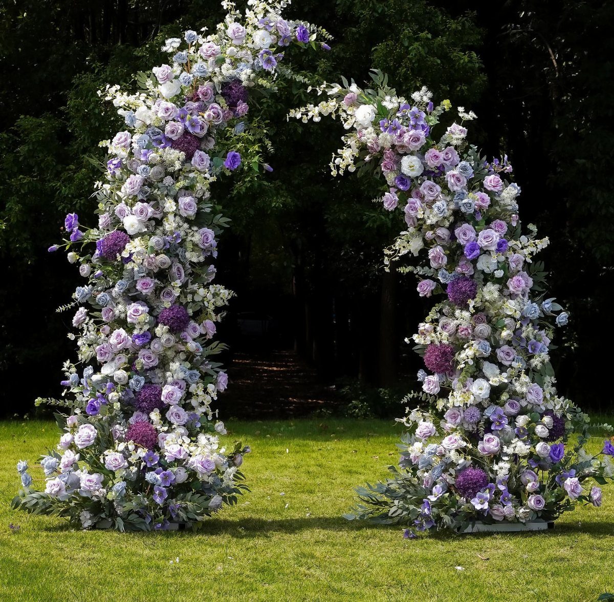 Outdoor Wedding Altar: 5 Ideas That Cost Less Than They Look 2 A large floral arch with purple and white flowers standing on a green lawn.