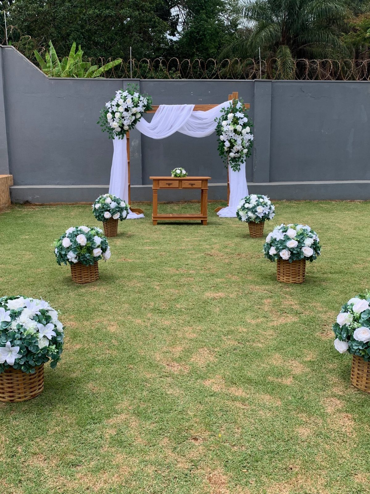 Outdoor Wedding Altar: 5 Ideas That Cost Less Than They Look 1 A wooden wedding arch with white fabric draping and white flowers on a green lawn.