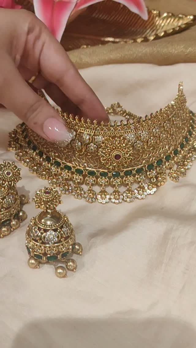Gold choker necklace with green gemstones and matching earrings on a cream fabric.