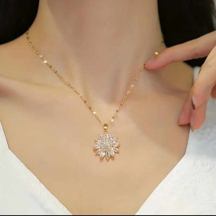 A gold necklace with a sparkling flower-shaped pendant worn around a person's neck.