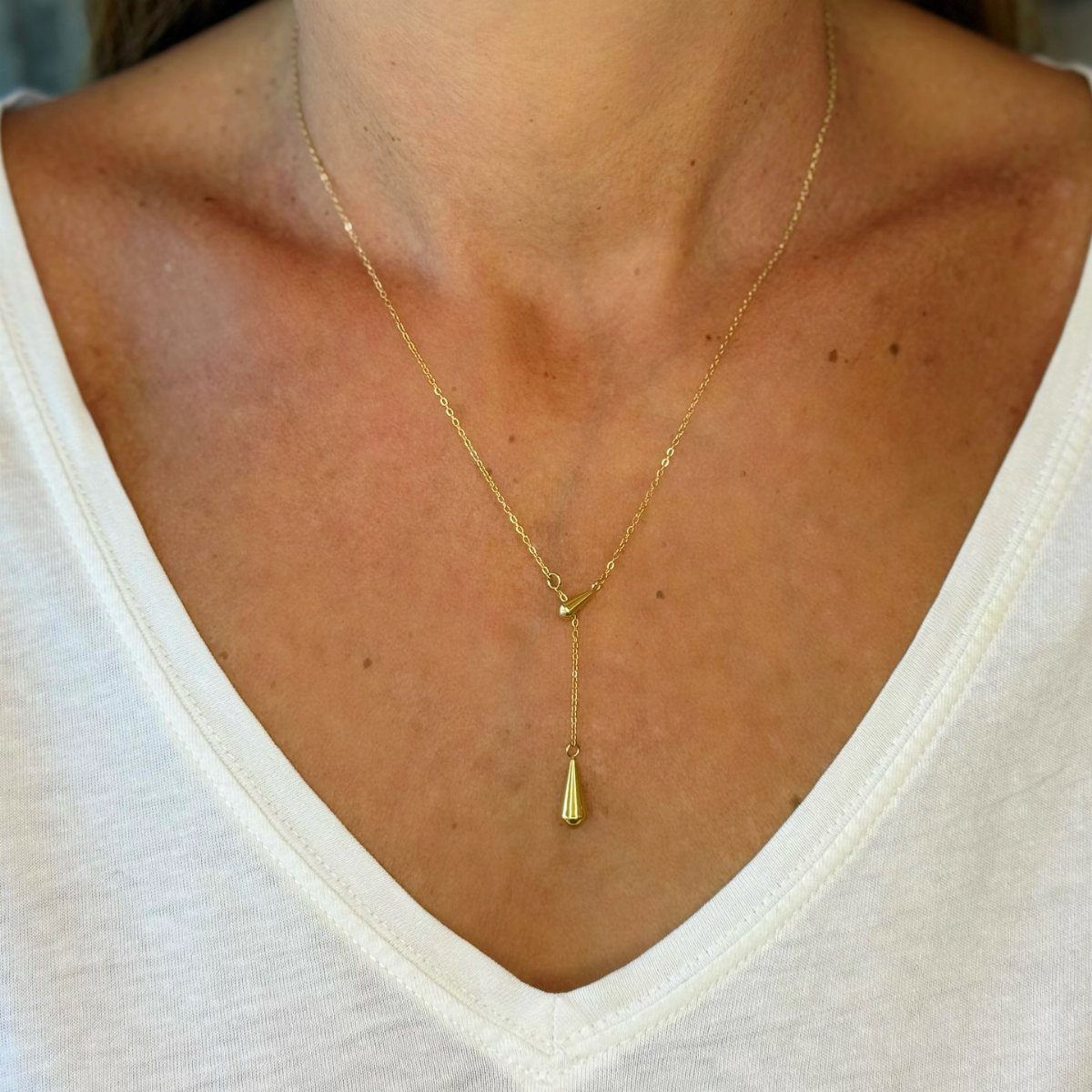 A gold lariat necklace with a teardrop pendant worn on a person's neck.