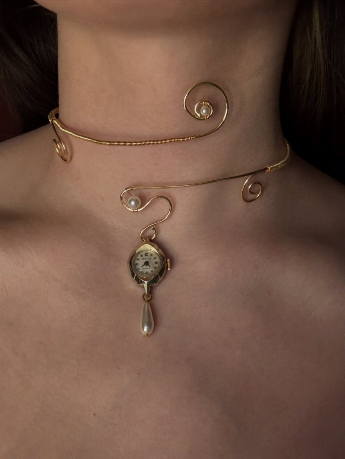 Gold wire choker necklace with abstract swirls, pearls, and a clock pendant on a person's neck.