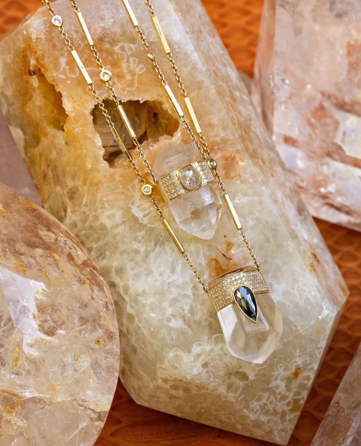 Two gold necklaces with clear gemstones resting on large translucent quartz crystals.