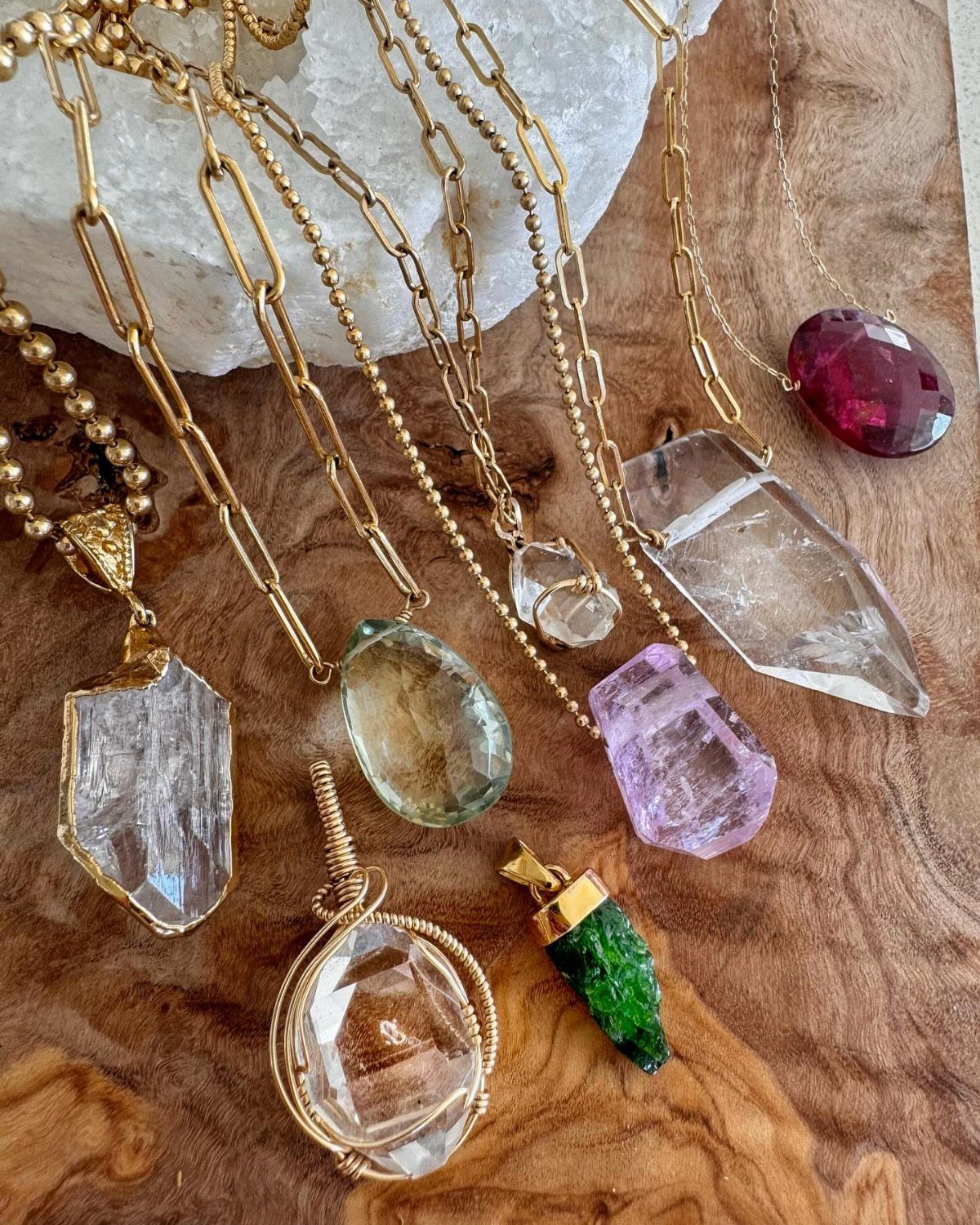 Gold necklaces with various colorful gemstone pendants resting on a wooden surface.