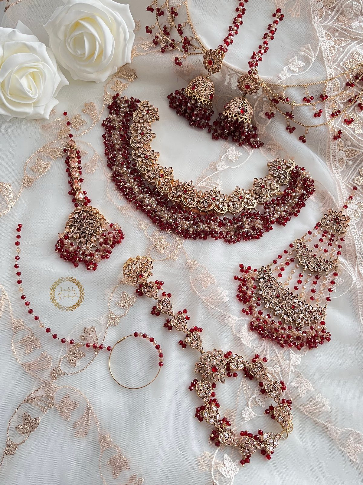Ornate gold jewelry set with red gemstones arranged on white lace fabric with roses.