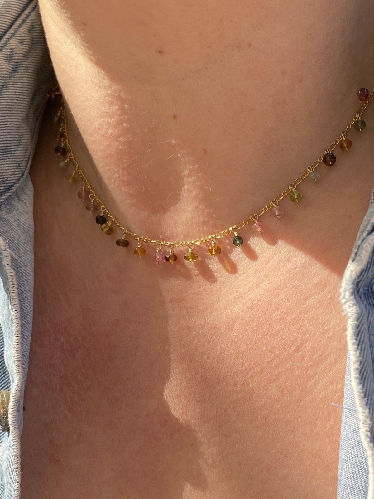 A gold chain necklace with many small, colorful hanging beads worn around a person's neck.
