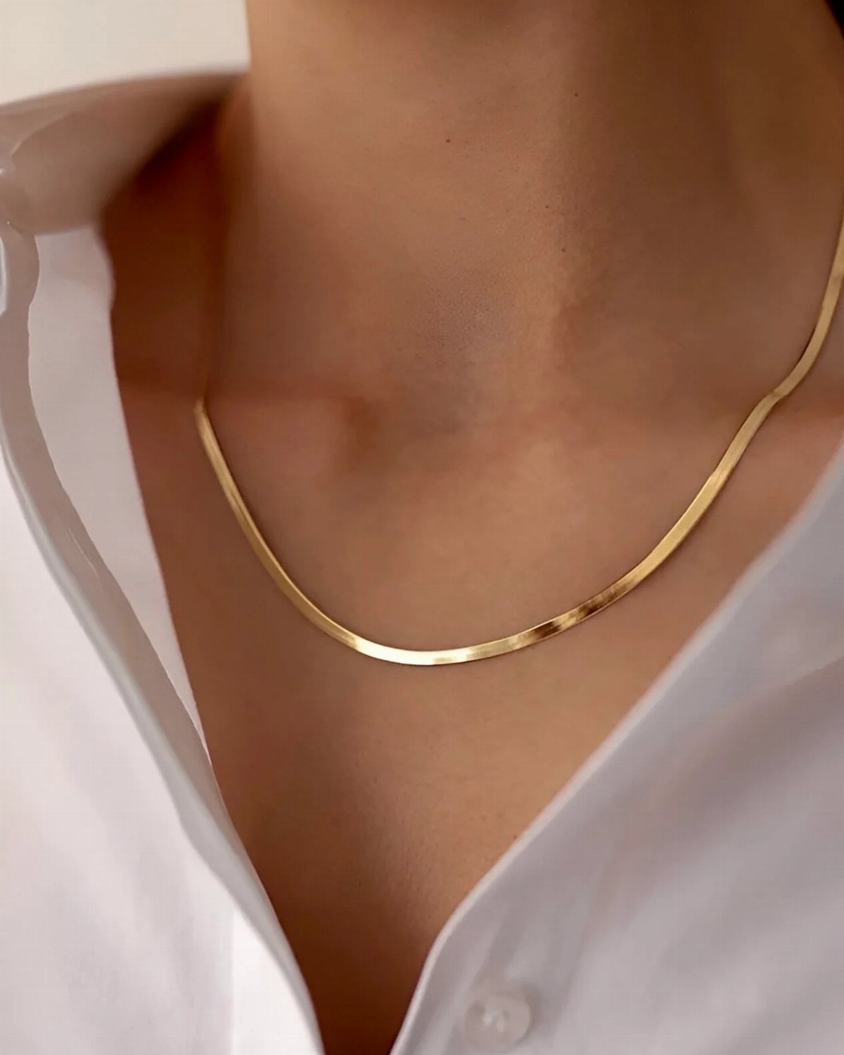 A smooth gold snake chain necklace worn around a person's neck with a white shirt.