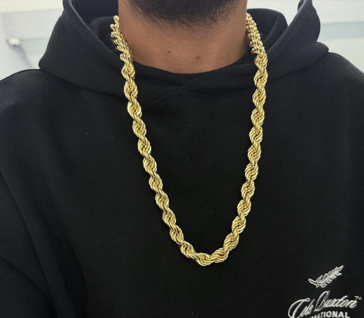 A thick gold twisted rope chain necklace worn over a black hoodie.