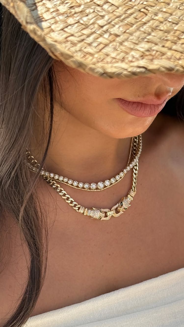 Two layered gold necklaces, one thin tennis chain and one thick cuban link, worn by a person.