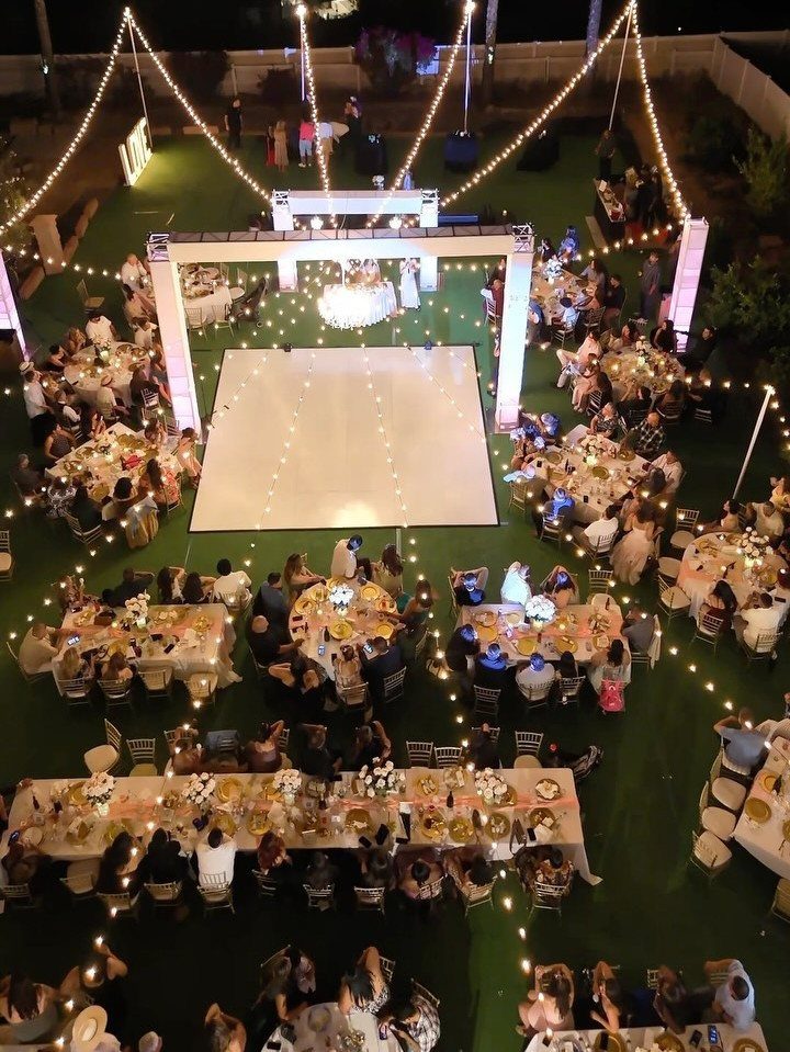 An outdoor evening wedding reception with guests seated at round tables surrounding a white dance floor.