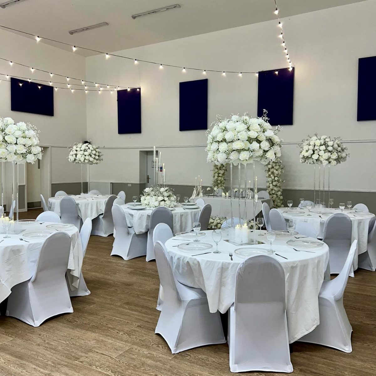 Round banquet tables with white linens and tall floral centerpieces in a large hall.