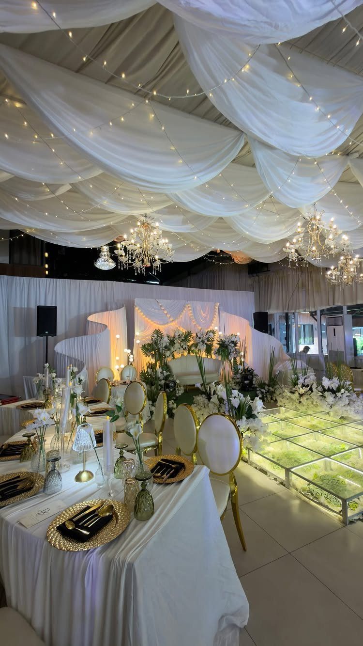 Elegant event reception setup with white draped ceilings, fairy lights, and decorated dining tables.