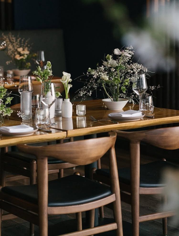 A set wooden dining table with elegant floral arrangements and glassware in a restaurant setting.