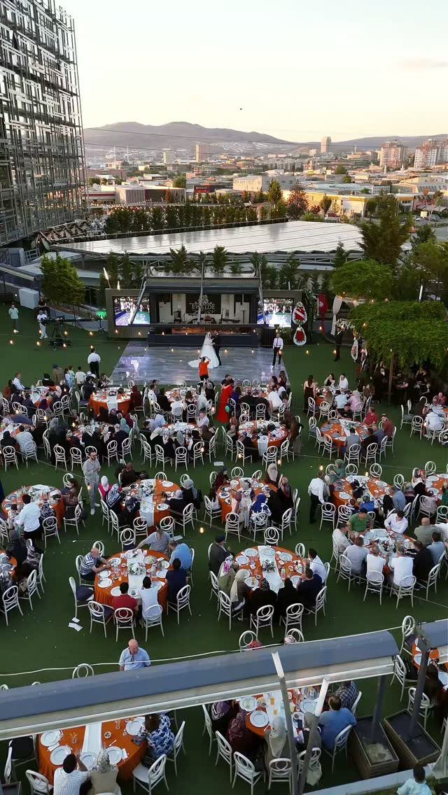 An outdoor rooftop banquet setup with many round tables overlooking a city skyline at dusk.