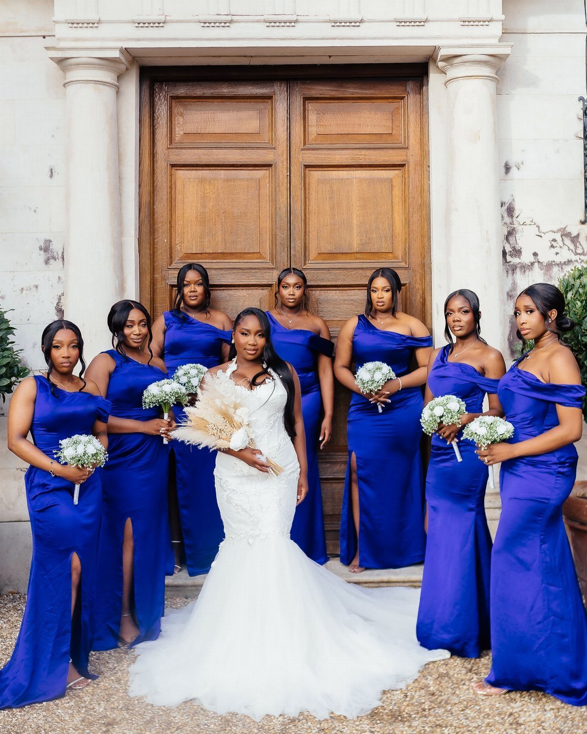 Seven bridesmaids in royal blue dresses posing with a bride in a white wedding gown.