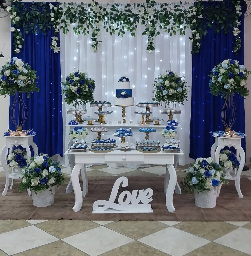 White dessert table decorated with blue and white flower arrangements and a blue tiered cake.