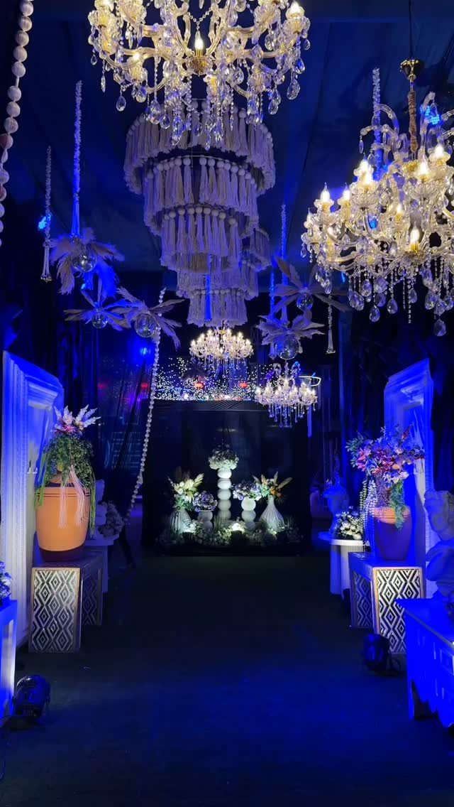 Crystal chandeliers and white tassels hang above a wedding venue illuminated with deep royal blue light.