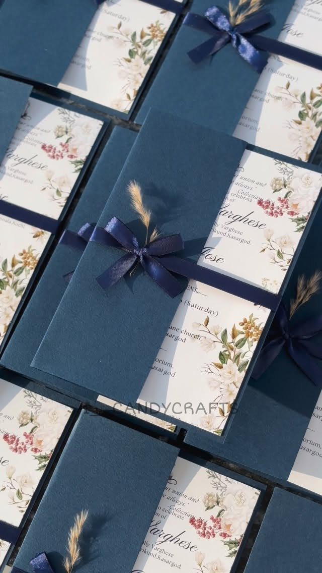 Royal blue wedding invitations with floral patterns and navy satin bows tied around them.