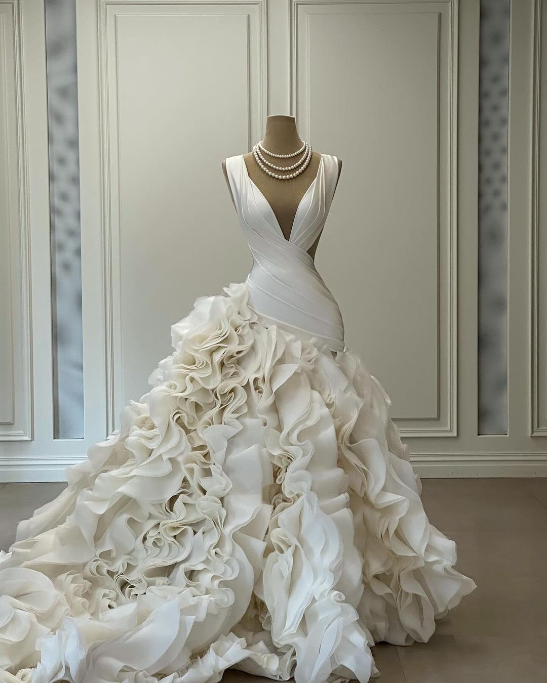 A white wedding dress with a sleek bodice and voluminous cascading ruffles on a mannequin.