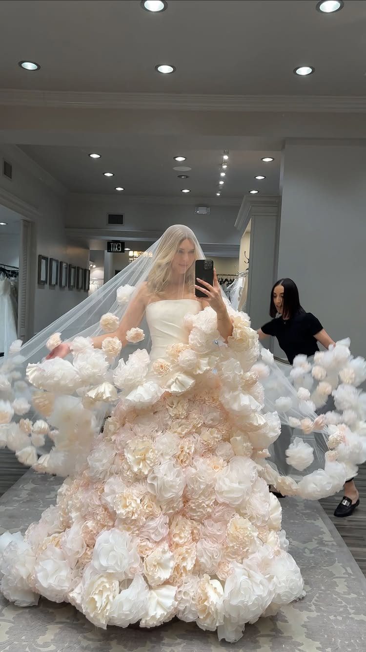 A woman wearing a voluminous wedding dress with large white floral ruffles while taking a selfie.