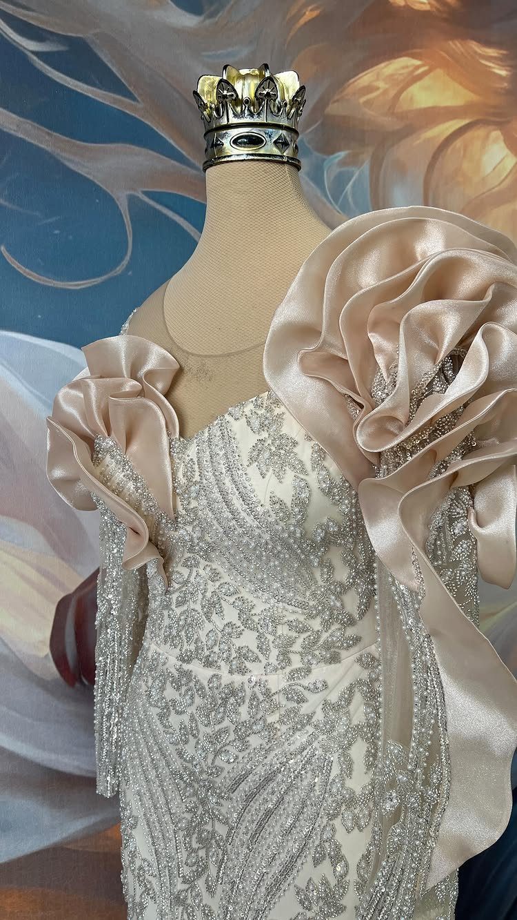 A beaded silver wedding dress on a mannequin with large champagne satin ruffles on the shoulders.
