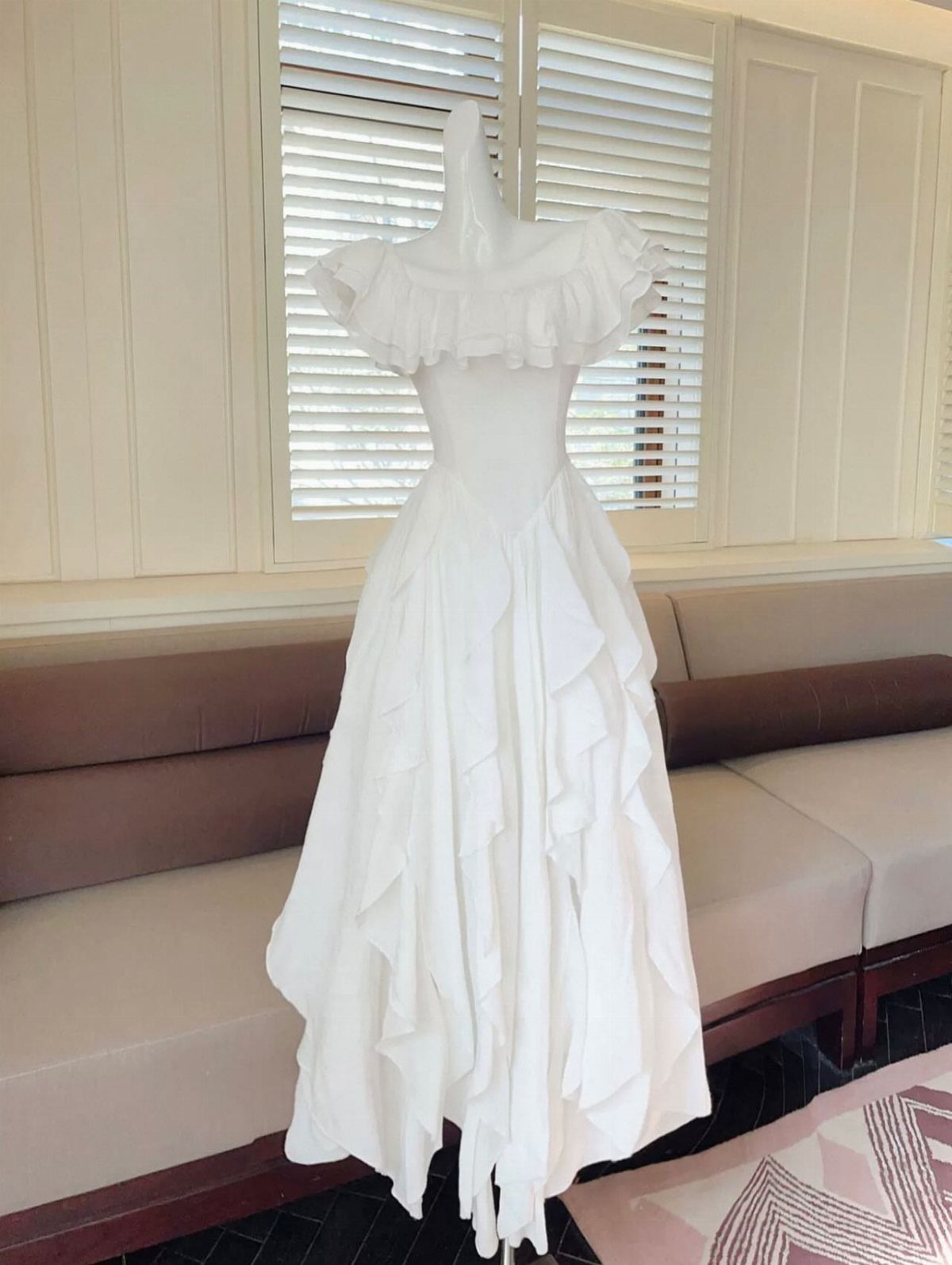 A white wedding dress with off the shoulder ruffles displayed on a mannequin.