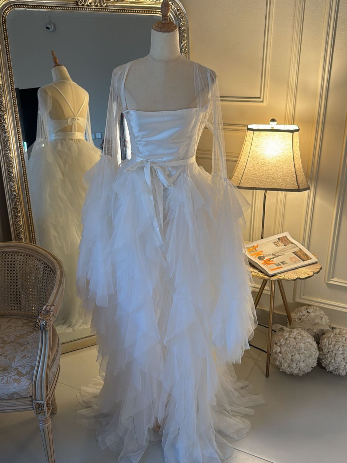 A white wedding dress with a satin bodice and voluminous tiered tulle ruffles on a mannequin.